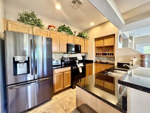A modern kitchen with stainless steel appliances, wooden cabinets, and a granite countertop. - Vistoso Condo #226C (Oro Valley)