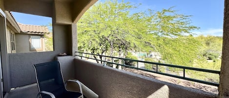 A balcony with a ceiling fan, a chair, and a patterned rug.