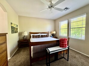 Ein Schlafzimmer mit einem Bett, zwei Nachttischlampen, einem Deckenventilator, einem Fenster mit Jalousien und einer roten Karodecke auf einer Bank.