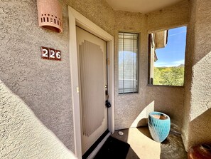 Eine strukturierte Außenwand mit einer Tür, auf der '226' steht, einem Fenster mit Jalousien und einem blauen Keramiktopf.
