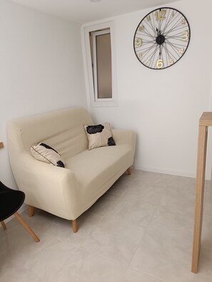 A room with a beige sofa, a black chair, a wooden table, and a wall clock. - Studio apartman  Belleza with jacuzzi and private parking (Zadar)