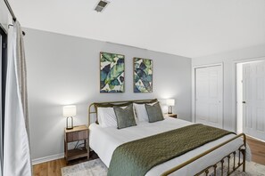 Un dormitorio con una cama, dos mesitas de noche, una mesita auxiliar, una puerta y dos cuadros colgados en la pared.