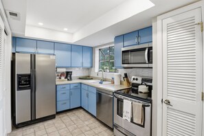 Una cocina compacta con gabinetes azules, electrodomésticos de acero inoxidable y un ventanal que proporciona luz natural.