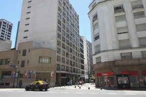 Vista de la calle con un edificio alto, un taxi y una tienda con un letrero rojo.