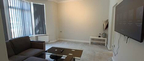 A living room with a sofa, a coffee table, a TV, and a small white shelf.