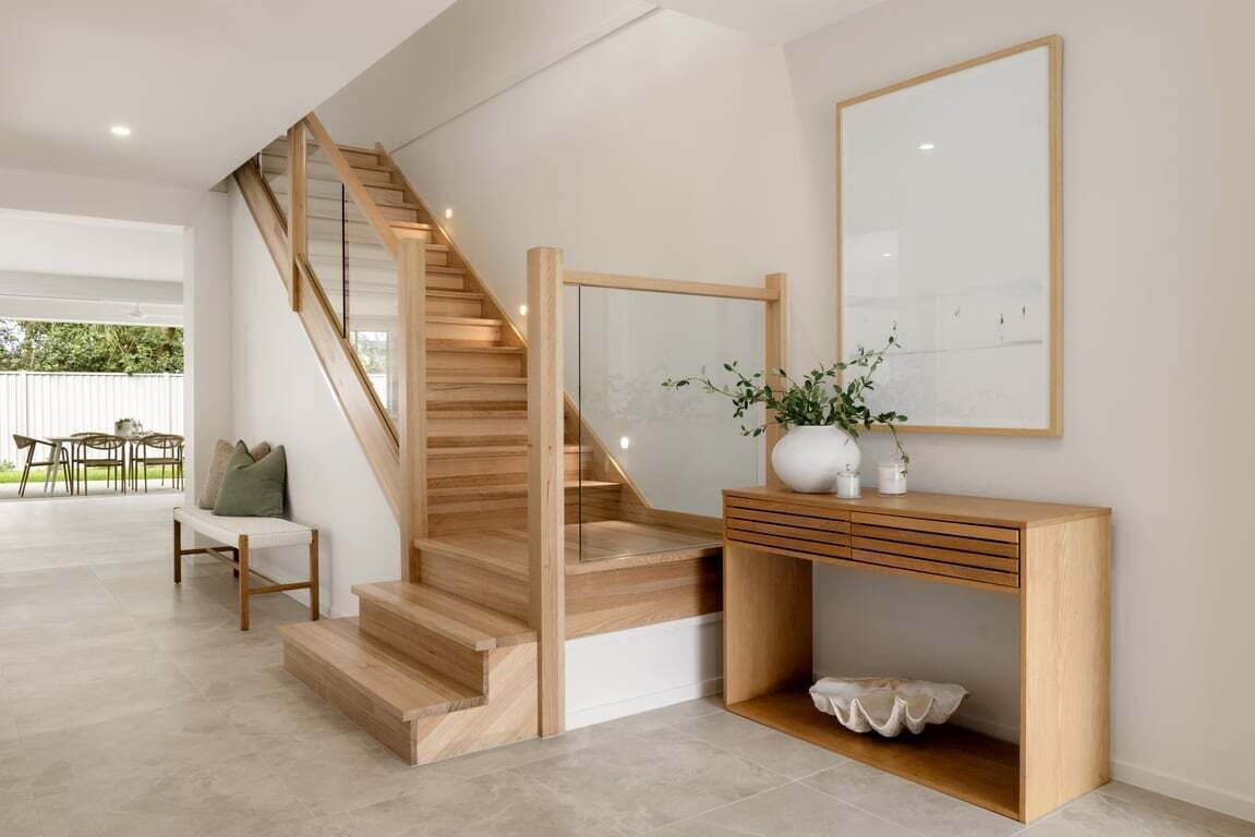 Een trap met houten treden en een glazen balustrade, die naar een verdieping leidt.