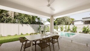 An outdoor patio with a table and chairs, a ceiling fan, and a swimming pool. - Mooloolaba Family 5 Bedroom Haven (Sunshine Coast)