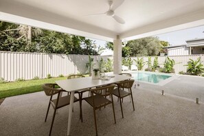 Eine Terrasse im Freien mit Tisch und Stühlen, einem Deckenventilator und einem Swimmingpool.