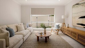 A modern living room with a sofa, coffee table, and a view of a balcony. - Mooloolaba Family 5 Bedroom Haven (Sunshine Coast)