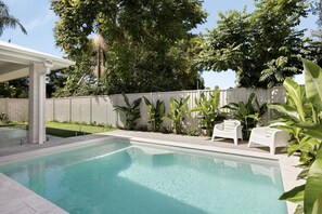 Ein rechteckiger Swimmingpool mit weißem Zaun und umlaufenden Pflanzen.