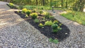 A gravel pathway with a garden bed containing various plants and flowers. - Stunning Lakefront Lodge with Dock and Hot Tub (Raymond)