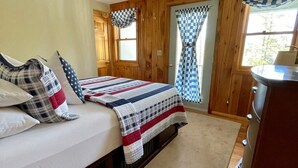 A bedroom with two beds, a ceiling fan, wooden walls, and a window with checkered curtains. - Stunning Lakefront Lodge with Dock and Hot Tub (Raymond)
