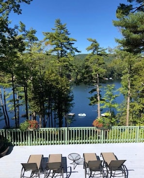A deck with outdoor seating overlooking a lake surrounded by trees.