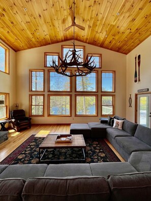 A spacious living room with a large chandelier, multiple windows, a leather chair, a sofa, and a coffee table.