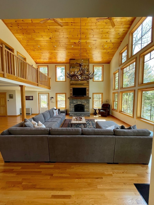 A spacious living room with a large sectional sofa, a stone fireplace, and a wooden ceiling.