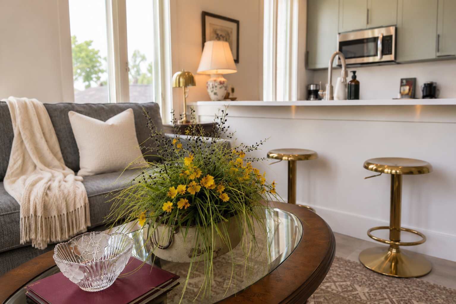 A living room with a sofa, a coffee table with a vase of flowers, and a kitchen in the background.