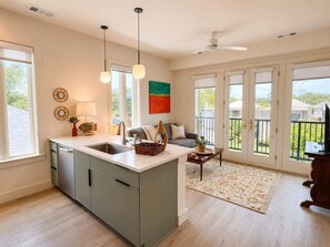 A modern kitchen with a central island, a dining area with a sofa, and a view through large sliding doors. - The Jardin Bloom Suite | Near Downtown (Savannah)