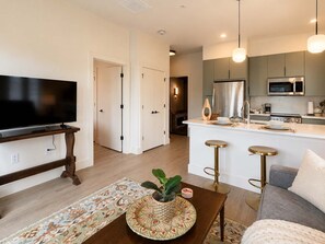 A modern living room with a flat-screen TV, a coffee table with a plant, and a patterned rug. - The Jardin Bloom Suite | Near Downtown (Savannah)