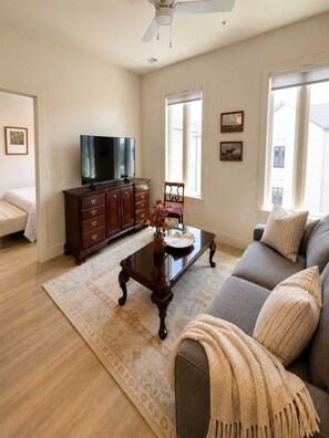 Un salon comprenant un canapé, une table basse, un téléviseur posé sur un meuble et un ventilateur de plafond.