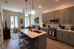 A modern kitchen with a central island, built-in appliances, and a dining area with a sofa and chairs. - The Jardin Petal Suite | Near Downtown (Savannah)