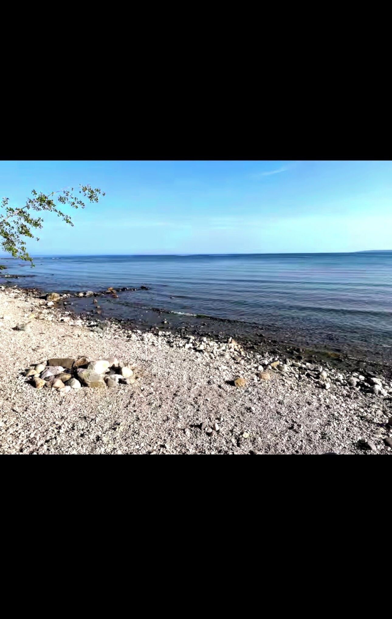 Una playa de guijarros con agua cristalina y un horizonte lejano.