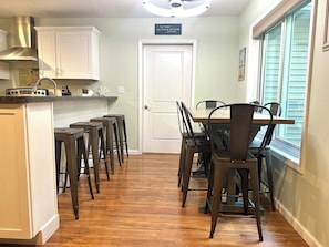 A kitchen with a dining table and chairs, a white door, and a window with blinds.