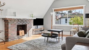 Ett modernt vardagsrum med en tegelbeklädd öppen spis, en platt-TV, ett runt soffbord och en soffa.