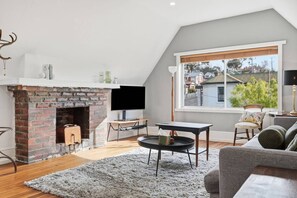 A modern living room with a brick fireplace, a flat-screen TV, a round coffee table, and a sofa. - Hill Street Hideaway (West Hobart)