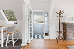 A room with a checkered floor, a white bench, a table with a view, and a fireplace. - Hill Street Hideaway (West Hobart)