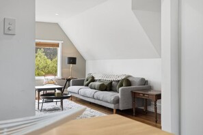 A modern loft-style living room with a grey sofa, a small round table, and a lamp. - Hill Street Hideaway (West Hobart)