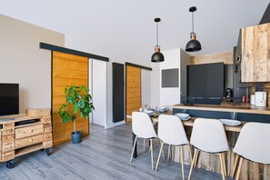 A modern kitchen with a dining area, wooden cabinets, and a potted plant. - Appartement Teilleria - Welkeys (Hendaye)