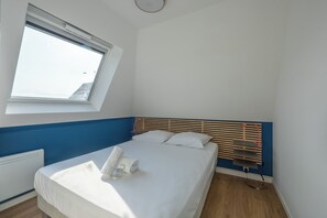 A single-bed room with a wooden headboard, a window with blinds, a radiator, and a bedside table with a lamp. - Le Balcon du Grand Cap - vue mer - Welkeys (Villers-sur-Mer)