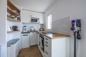 A compact kitchen with white cabinets, a microwave, a coffee maker, and a Dyson vacuum cleaner. - Le Balcon du Grand Cap - vue mer - Welkeys (Villers-sur-Mer)