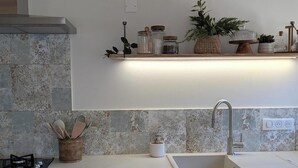Een keuken met een modern ontwerp, voorzien van een roestvrijstalen kraan, een houten plank met potten en planten, en een betegelde spatwand.