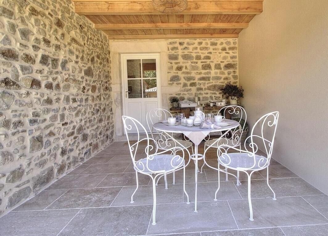 Un patio de paredes de piedra con una mesa redonda y sillas de metal blanco.