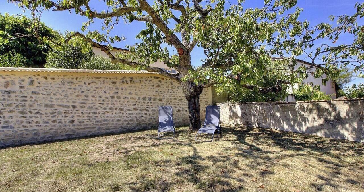 A stone wall, a tree, and two chairs in a courtyard.