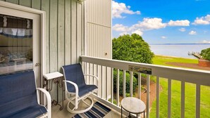 A balcony with a view of a body of water, a small table, a chair, and a bench. - RSC203 - Wander Mint Soundfront condo with sunset views (Manteo)