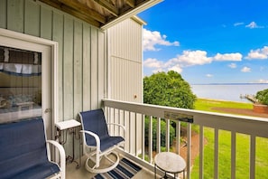 A balcony with a view of a body of water, a small table, a chair, and a bench. - RSC203 - Wander Mint Soundfront condo with sunset views (Manteo)