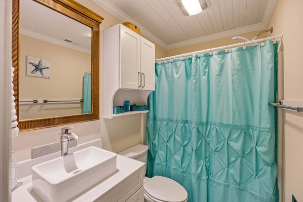 A bathroom with a white sink, a toilet, a mirror with a gold frame, and a teal shower curtain. - RSC203 - Wander Mint Soundfront condo with sunset views (Manteo)