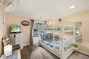 A child's bunk bed with a floral bedspread, a television on a dresser, and a window with curtains. - RSC203 - Wander Mint Soundfront condo with sunset views (Manteo)