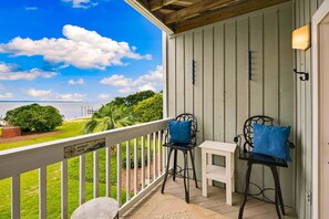 Een balkon met uitzicht op het water, twee stoelen, een klein tafeltje, en een bord met de tekst 'WANDER MORE'.