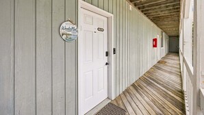 A corridor with a wooden floor, a white door with a welcome sign, and a fire extinguisher on the wall. - RSC203 - Wander Mint Soundfront condo with sunset views (Manteo)