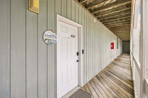 A corridor with a wooden floor, a white door with a welcome sign, and a fire extinguisher on the wall. - RSC203 - Wander Mint Soundfront condo with sunset views (Manteo)