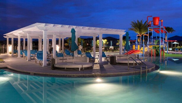 A poolside area with lounge chairs and a covered seating area, a children's play structure, and a pool. - Designer 8BR Villa | Private Pool, Spa & Lanai (Kissimmee)