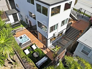 A modern two-story building with a patio area featuring a hot tub, outdoor seating, and a small fire pit. - Golden Hill 7BR Retreat with Private Hot Tub (San Diego)