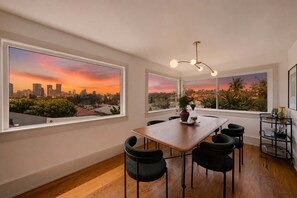Comedor con vista a la ciudad, una mesa de madera, sillas negras y una lámpara moderna.