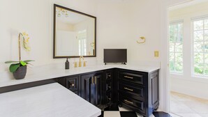 A bathroom with a white vanity, black cabinets, a gold faucet, a large mirror, and a potted orchid.