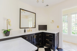 A bathroom with a white vanity, black cabinets, a gold faucet, a large mirror, and a potted orchid.