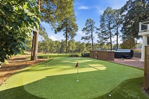 A miniature golf course with a brick patio, a grill, and trees in the background.