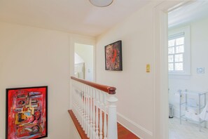 A hallway with a staircase, a painting on the wall, and a bathroom visible through an open door.